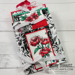 A handmade floral card features red and pink flowers with green leaves on white backgrounds, layered over black and white leafy paper. The card is tied with white ribbon and accented with a strip of red. The words “THINKING” and “Patty Bennett pattystamps.com” appear. To read more, visit Patty Stamps (pattystamps.com)