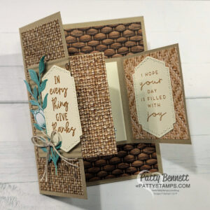 A handmade, textured greeting card with woven and basket patterns opens in two panels. The left panel says “IN everything GIVE thanks,” adorned with blue-green leaves and twine. The right reads “I HOPE YOUR DAY IS FILLED WITH joy.” Both have stitched-edge beige tags. To read more, visit Patty Stamps (pattystamps.com)