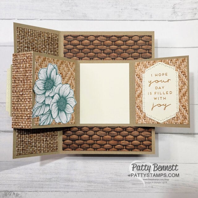 A handmade card with woven brown patterns, featuring a floral illustration on the left and a white panel on the right that says "Hope your day is filled with joy" in gold. The card is displayed on a light wood background. "Patty Bennett" watermark is in the lower right. To read more, visit Patty Stamps (pattystamps.com)