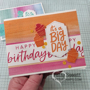 Two handmade birthday cards, each decorated with a “It’s a Big Day” greeting from Stampin UP! Around it All and With You in Mind stamp sets, striped backgrounds in teal or orange tones, cupcake cutouts, and sequins. A package of starburst sequins in yellow, pink, and white sits beside the cards on a grid-patterned surface. To read more, visit Patty Stamps (pattystamps.com)