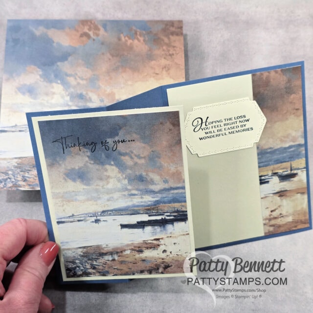 A hand holds an open sympathy card with a serene painting of boats on water under a cloudy sky. The front reads "Thinking of you..." and inside is a message: "Hoping the loss you feel right now will be eased by wonderful memories. To read more, visit Patty Stamps (pattystamps.com)