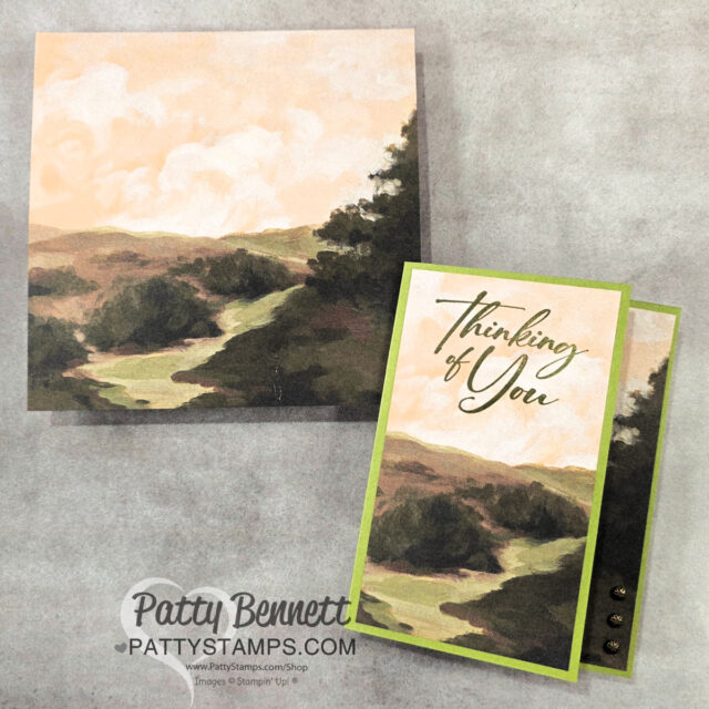 A handmade card and matching envelope with a serene painted landscape of rolling hills, grassy fields, and a soft pastel sky. The card, bordered in green, reads "Thinking of You" in elegant script, and has three metallic embellishments on the right edge. To read more, visit Patty Stamps (pattystamps.com)