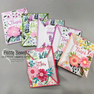 Seven colorful, floral handmade greeting cards are arranged on a gray surface. Each card features layered paper flowers and foliage, with messages like “Thank you,” “Best Wishes,” “Thinking of You,” and “Happy Birthday.” The PattyStamps.com logo appears on the left. To read more, visit Patty Stamps (pattystamps.com)