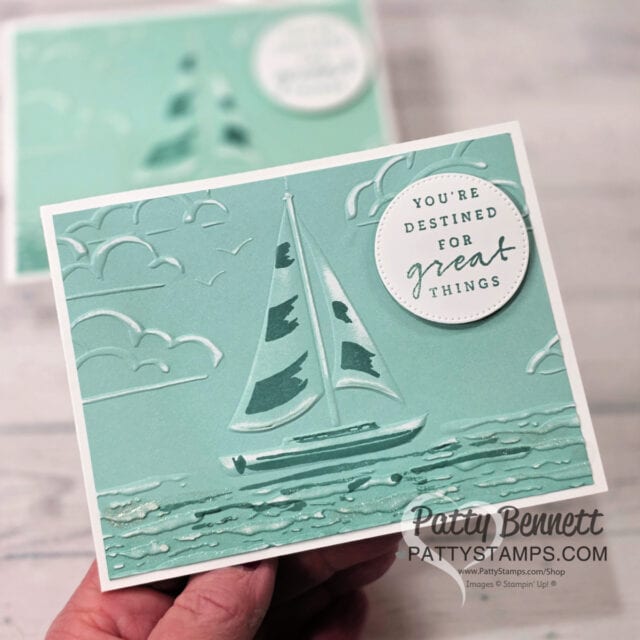 A hand holds a teal embossed greeting card featuring a sailboat on water with clouds in the sky. A white circle in the top right reads, "You're destined for great things." The card is displayed against a blurred background. To read more, visit Patty Stamps (pattystamps.com)