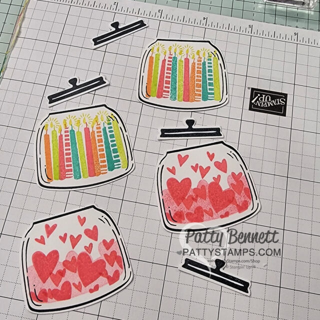Four jar-shaped paper cutouts are shown on a grid mat; two are decorated with colorful birthday candles, and two with pink and red hearts. Black jar lid cutouts are placed nearby. A transparent Stampin’ Up! block and a PattyStamps watermark are visible. To read more, visit Patty Stamps (pattystamps.com)