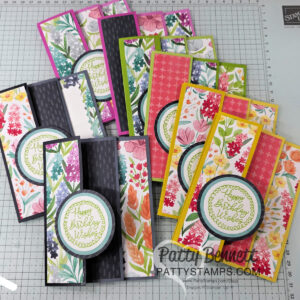 A collection of handmade floral-themed birthday cards, each featuring colorful patterned paper, layered circle accents with "Happy Birthday Wishes" in green script, and various vibrant backgrounds, arranged on a gridded crafting mat. To read more, visit Patty Stamps (pattystamps.com)