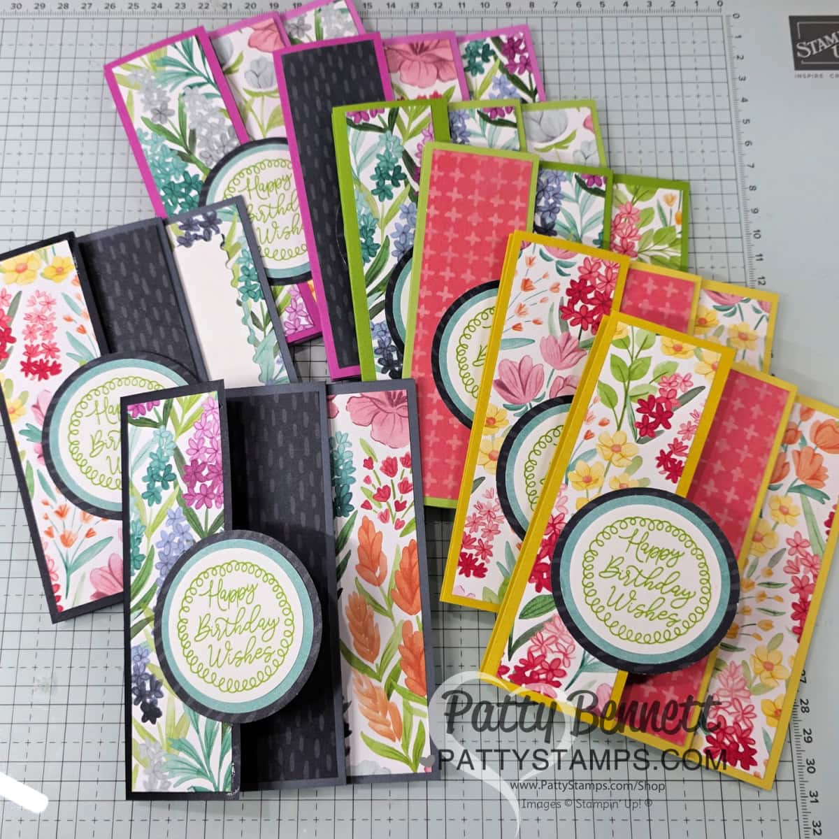A collection of handmade floral-themed birthday cards, each featuring colorful patterned paper, layered circle accents with "Happy Birthday Wishes" in green script, and various vibrant backgrounds, arranged on a gridded crafting mat. To read more, visit Patty Stamps (pattystamps.com)