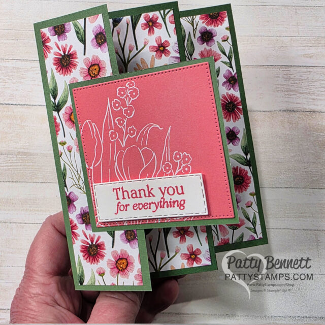 A handmade floral thank-you card with a tri-fold design. The card features pink and white flowers on side panels and a pink center with embossed white flowers. The message “Thank you for everything” is stamped in red on a white label. A hand holds the card. To read more, visit Patty Stamps (pattystamps.com)