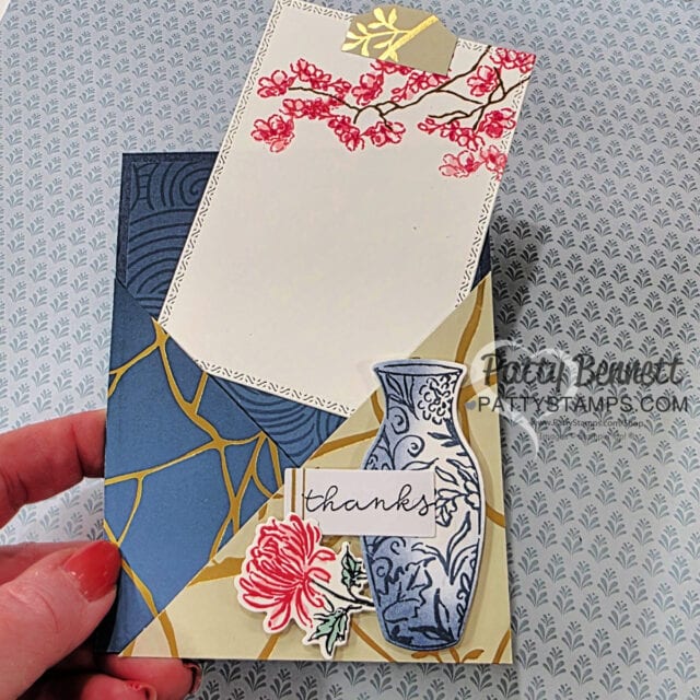 A handmade “thanks” card with a blue and gold geometric background, a blue-and-white vase illustration, a red flower, and a pull-out white note decorated with red blossoms. A hand with red nail polish holds the card. The creator’s watermark is visible. To read more, visit Patty Stamps (pattystamps.com)