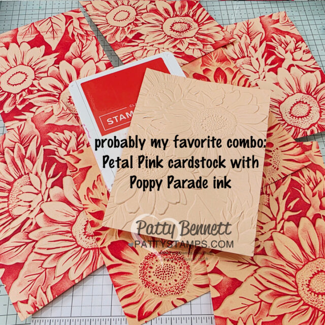 Several sheets of cardstock feature large sunflower designs stamped in bright red ink on a peach background. A white and red ink pad and a plain embossed peach card sit on top. Text in black reads: "probably my favorite combo: Petal Pink cardstock with Poppy Parade ink. To read more, visit Patty Stamps (pattystamps.com)