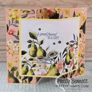 A handmade, multi-fold greeting card features watercolor pears, yellow and pink flowers, and green leaves. The center reads, "A good friend is a gift," accented with a bow and gems. Background is floral, with "Patty Bennett PATTYSTAMPS.com" on the front. To read more, visit Patty Stamps (pattystamps.com)