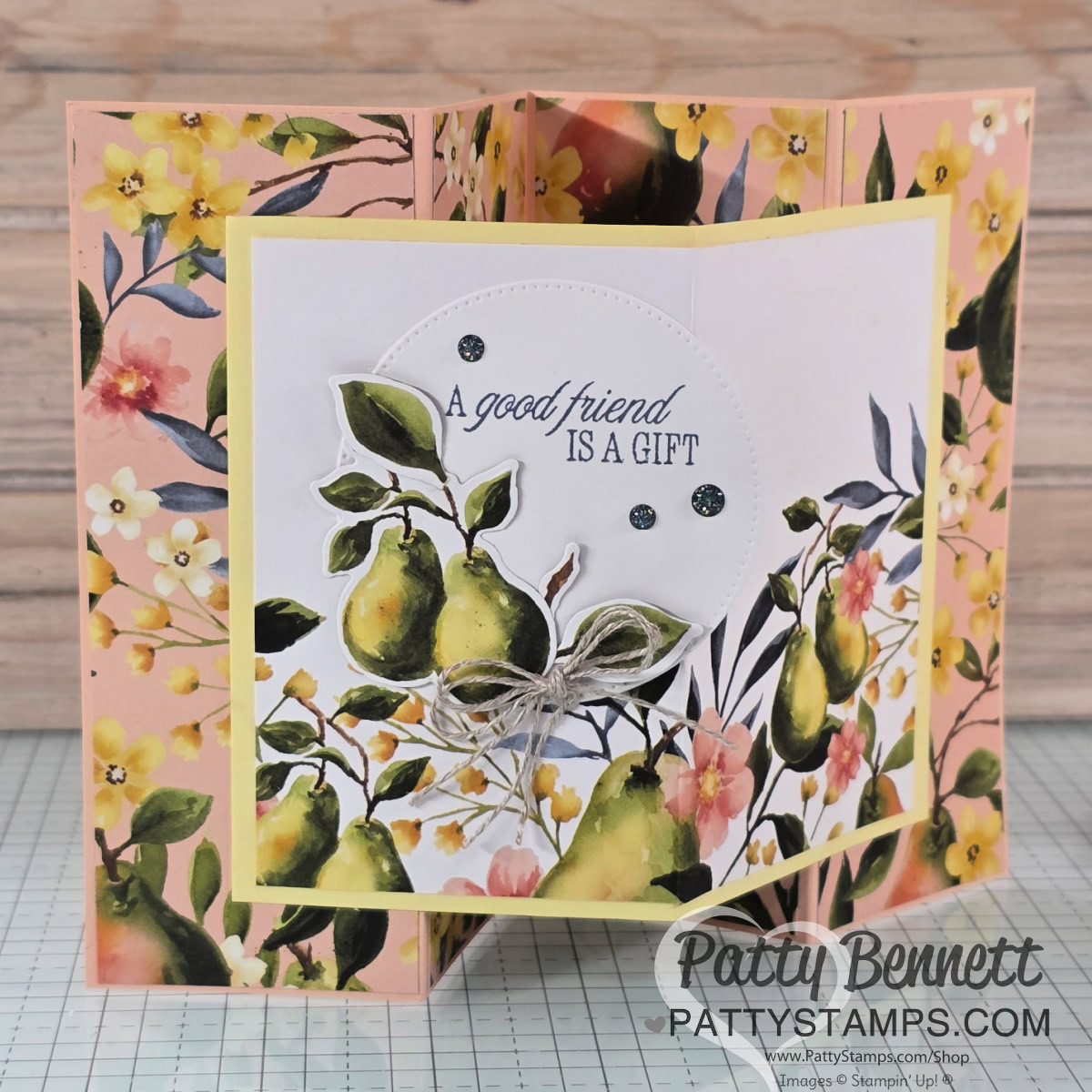 A handmade, multi-fold greeting card features watercolor pears, yellow and pink flowers, and green leaves. The center reads, "A good friend is a gift," accented with a bow and gems. Background is floral, with "Patty Bennett PATTYSTAMPS.com" on the front. To read more, visit Patty Stamps (pattystamps.com)