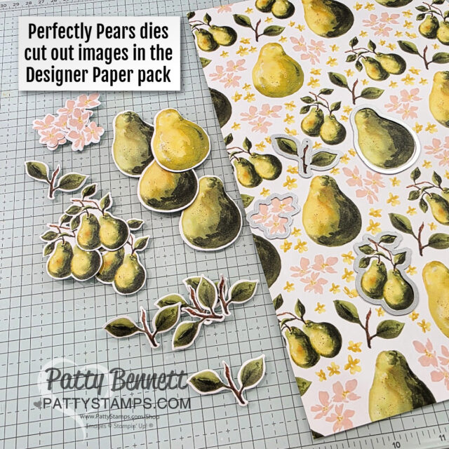A sheet of decorative paper with a pattern of pears and pink flowers lies on a grid work surface. Cut-out pear fruit and leafy branch shapes are arranged nearby—perfect for pocket card projects with Stampin' Up! products by pattystamps. To read more, visit Patty Stamps (pattystamps.com)