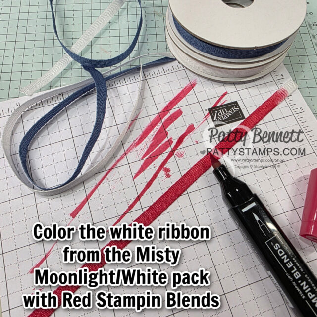 A workspace with a grid mat shows blue and white ribbon rolls, a piece of white ribbon being colored red with a Red Stampin’ Blends marker, and a stamped ink pad. Text reads: "Color the white ribbon from the Misty Moonlight/White pack with Red Stampin Blends. To read more, visit Patty Stamps (pattystamps.com)