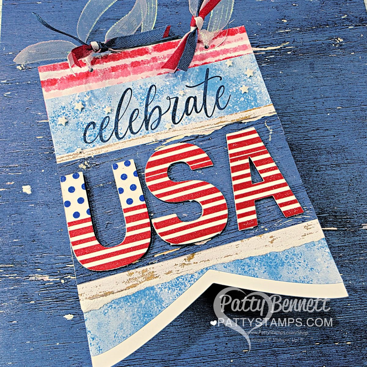 A festive banner with "celebrate USA" in blue script and bold letters, decorated in stars and red, white, and blue stripes. Blue ribbons are tied at the top, and the banner sits on a textured blue wooden background. "Patty Bennett" watermark at the bottom. To read more, visit Patty Stamps (pattystamps.com)