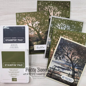 Four handmade greeting cards featuring scenic stamped tree and landscape designs are displayed in a fan shape. Two Stampin’ Up! ink pads in “Secret Sea” and “Mossy Meadow” colors are in the foreground. A small “hello” tag and a “Hi There!” card are also visible. To read more, visit Patty Stamps (pattystamps.com)