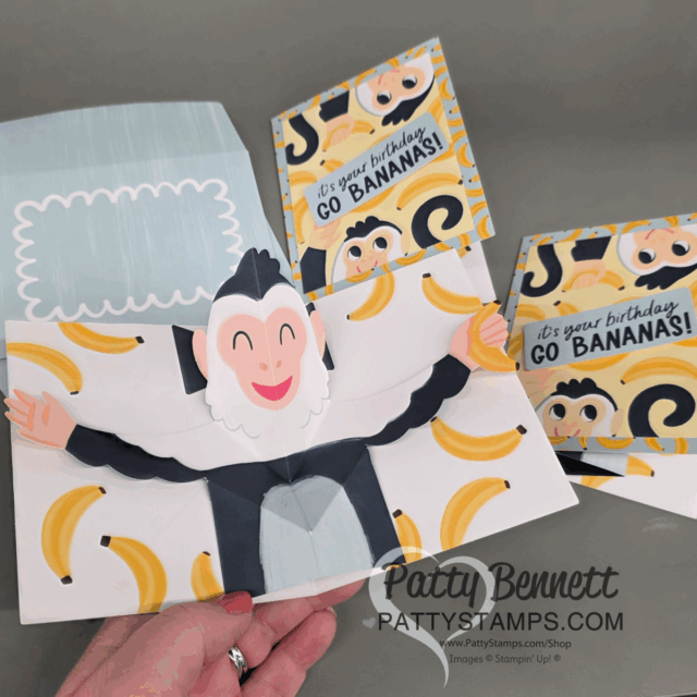 A hand holds a pop-up birthday card featuring a smiling cartoon monkey with outstretched arms. Two matching flat cards in the background say, “It’s your birthday! Go BANANAS!” with monkey faces and banana illustrations on a yellow and black design. To read more, visit Patty Stamps (pattystamps.com)