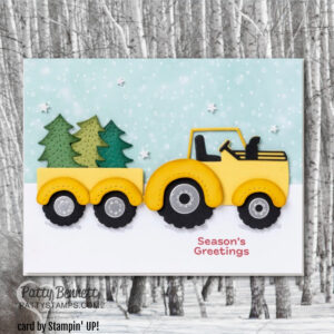 A handmade card shows a yellow tractor with a trailer carrying two green trees on snowy ground. The background is blue with white dots resembling snow, and "Season’s Greetings" is printed in red at the bottom right. Snowflakes are scattered in the sky. To read more, visit Patty Stamps (pattystamps.com)