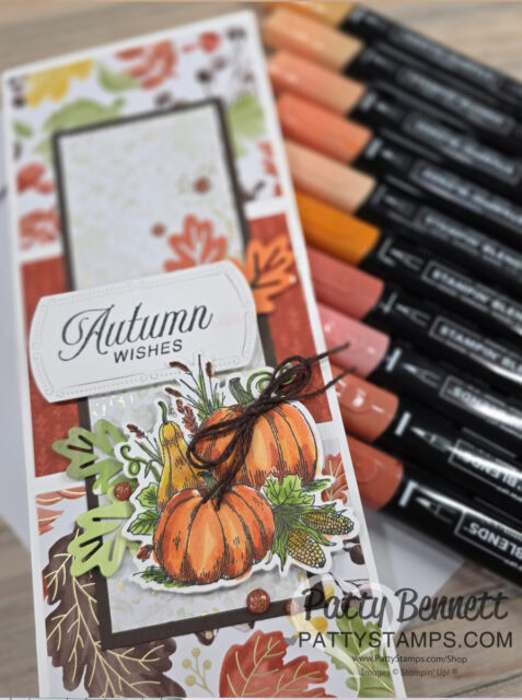 A handmade “Autumn Wishes” card decorated with pumpkins, leaves, and acorns sits beside orange, brown, and yellow alcohol markers. The card features layered autumn-themed papers and a twine bow. “Patty Bennett” and website text appear in the corner. To read more, visit Patty Stamps (pattystamps.com)