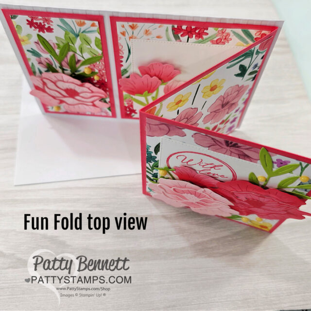 A handmade floral greeting card with a "fun fold" design is shown from a top view. The card features bright pink and red flowers, green leaves, gold embellishments, and a "With Love" sentiment. The Patty Bennett/PattyStamps logo appears at the bottom. To read more, visit Patty Stamps (pattystamps.com)