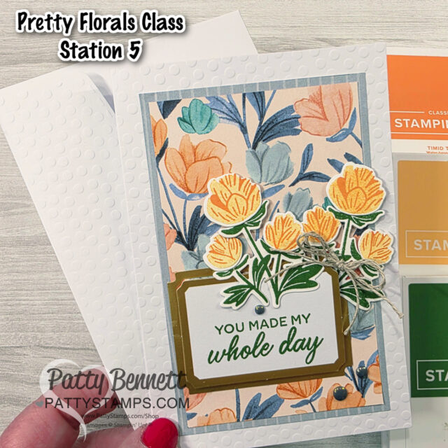 A handmade floral greeting card with orange and yellow flowers and green leaves is layered over a textured white background. The card reads "YOU MADE MY whole day." Colored paper swatches and "Pretty Florals Class Station 5" text appear above the card. To read more, visit Patty Stamps (pattystamps.com)