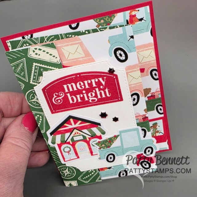 A hand holds a festive greeting card featuring “merry & bright” in white letters on a red label. The card has illustrations of blue trucks, letters, postage stamps, and a holiday house, all in Christmas colors and patterns. To read more, visit Patty Stamps (pattystamps.com)