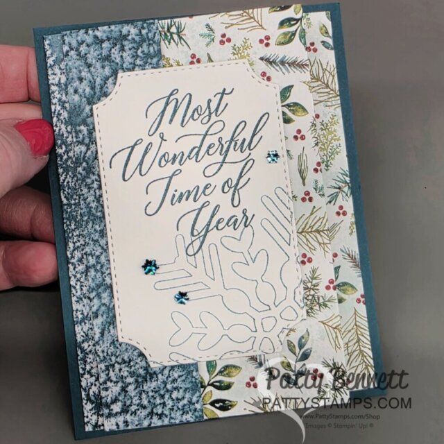 A handmade holiday card with blue and white snowy and botanical-patterned papers. Centered is a cream panel with ornate edges, reading "Most Wonderful Time of Year" in elegant script, with blue gem embellishments and a delicate snowflake outline below the text. To read more, visit Patty Stamps (pattystamps.com)