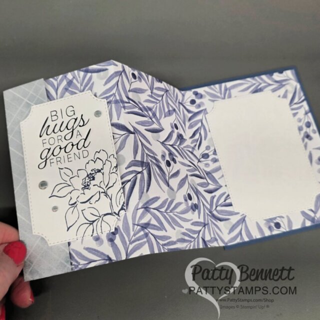 A handmade greeting card with blue and white floral designs, opened to show two panels. The left panel has a message, "Big hugs for a good friend," with a floral illustration and decorative gems. The right panel has a blank white space for a personal note. To read more, visit Patty Stamps (pattystamps.com)