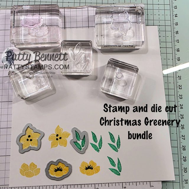 A crafting workspace with four clear stamps on blocks, stamped yellow flowers, green leaves, and matching gray metal dies. "Stamp and die cut Christmas Greenery bundle" is written on the white paper, with crafting tools visible around the workspace. To read more, visit Patty Stamps (pattystamps.com)