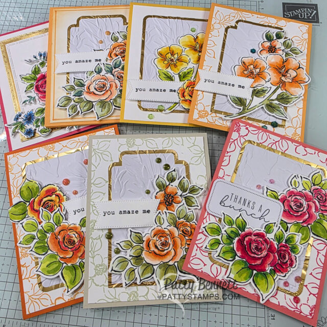A collection of handmade greeting cards featuring colorful, hand-colored floral designs. Each card includes vibrant flowers, green leaves, embossed backgrounds, and stamped sentiments such as “you amaze me” or “thanks.” The cards are arranged on a craft table. To read more, visit Patty Stamps (pattystamps.com)