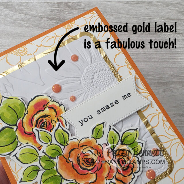 Embossed Gold Labels A handmade card with orange and yellow roses, green leaves, and peach enamel dots. The background has embossed white paper with a gold border. A white label reads "you amaze me." An arrow points to the label with the text "embossed gold label is a fabulous touch!. To read more, visit Patty Stamps (pattystamps.com)