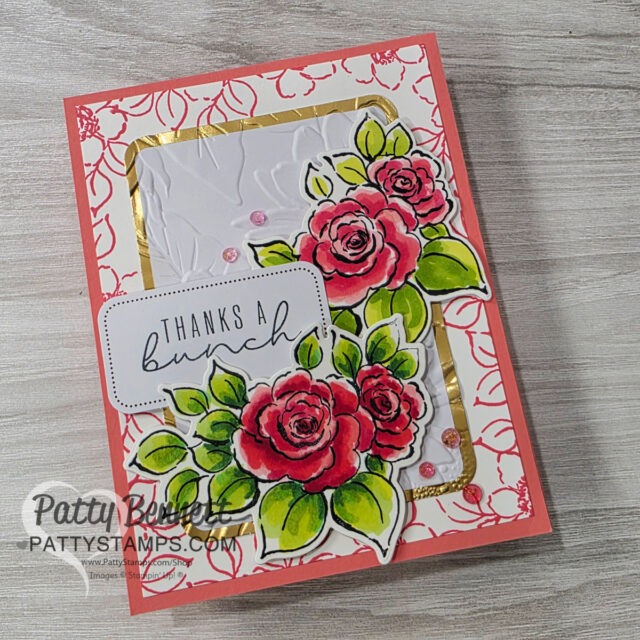 A handmade card with pink and red roses, green leaves, and a gold-bordered white panel. The card reads "THANKS A bunch" in black script. Pink gems are scattered, and the background features a pink floral pattern. "PattyStamps.com" is watermarked. To read more, visit Patty Stamps (pattystamps.com)