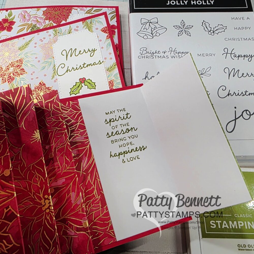 A handmade Christmas card with red and gold poinsettia designs is open, revealing the inside message: "May the spirit of the season bring you hope, happiness & love." Stamps, stamp sets, and another card with “Merry Christmas” are nearby. To read more, visit Patty Stamps (pattystamps.com)