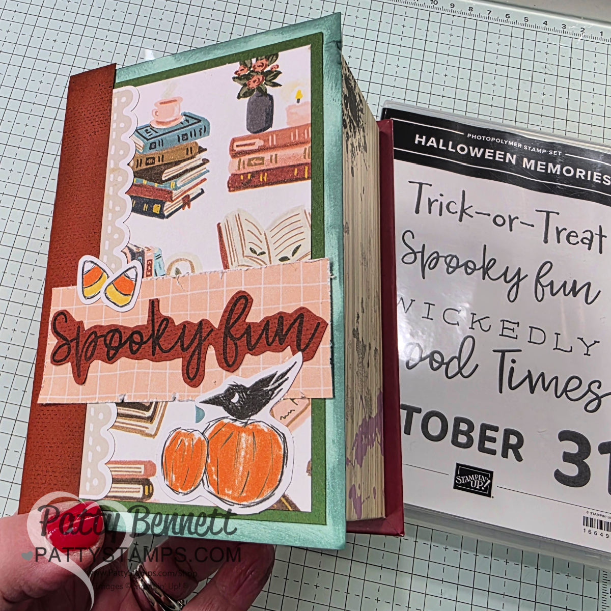 A handmade, Halloween-themed scrapbook features a decorated cover with illustrations of stacked books, pumpkins, and glasses. The words "Spooky fun" are written in script. To the right is a photopolymer stamp set labeled "Trick-or-Treat Spooky fun Wickedly Good Times OCTOBER 31. To read more, visit Patty Stamps (pattystamps.com)