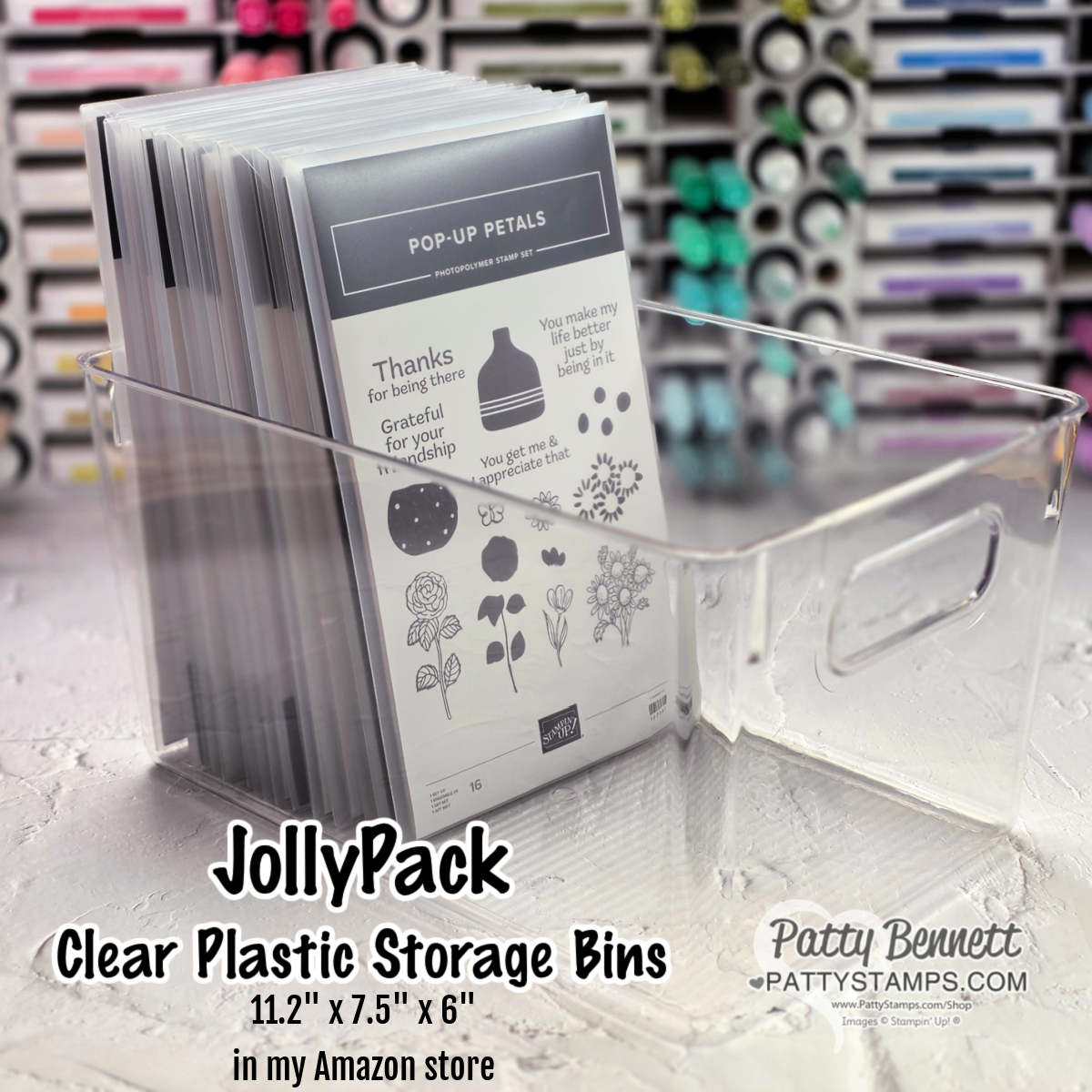 A clear plastic storage bin holds several upright crafting stamp sets labeled "Pop-Up Petals." The bin has a handle cutout and sits on a marble surface. Text on the image advertises "JollyPack Clear Plastic Storage Bins" with dimensions and Amazon store info. To read more, visit Patty Stamps (pattystamps.com)