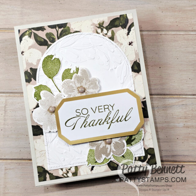 A handmade thank-you card features a floral background with green leaves and white flowers, an embossed white arch, and a layered tag reading "SO VERY Thankful" in black and gold text. Some flowers have pearl centers. “Patty Bennett” is printed on the lower right. To read more, visit Patty Stamps (pattystamps.com)