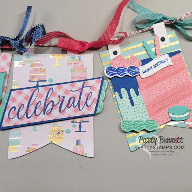 A festive handmade birthday banner features pastel pennants with cakes and macarons. One pennant has “celebrate” in script, bordered in blue, while another has layered cake images, ribbon, and a “HAPPY BIRTHDAY” tag. Ribbons tie the banner together at the top. To read more, visit Patty Stamps (pattystamps.com)