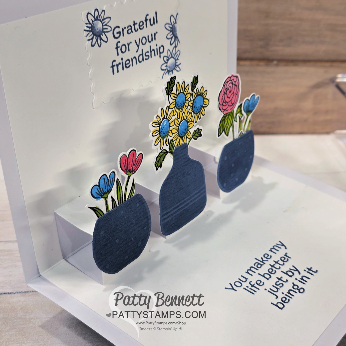 A handmade pop-up card shows three dark blue vases with colorful flowers. The card reads, "Grateful for your friendship" at the top and "You make my life better just by being in it" at the bottom. The card is signed “Patty Bennett.”. To read more, visit Patty Stamps (pattystamps.com)