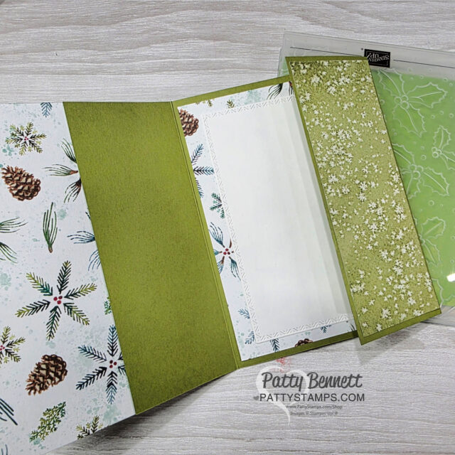 A handmade holiday card is open to display multiple green and white panels. The left panel has pinecones and branches, the center is green with a white stitched frame, and the right panel is green with a snowflake pattern. “Patty Bennett @ PattyStamps.com” is printed below. To read more, visit Patty Stamps (pattystamps.com)