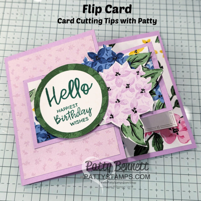 A handmade flip card on a grid background. The card is lavender with floral patterns and a green-bordered circle that says, "Hello HAPPIEST BIRTHDAY WISHES." Text above reads, "Flip Card Card Cutting Tips with Patty." The card displays layered flower designs. To read more, visit Patty Stamps (pattystamps.com)