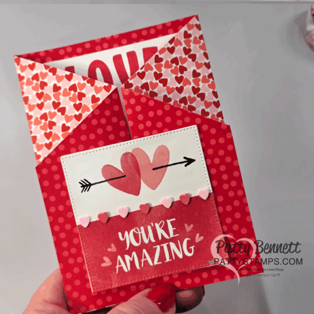 A hand holds a handmade Fun Fold Card with red and pink heart patterns. The card has layered pockets, heart and arrow designs, and the message "YOU'RE AMAZING." Perfect for card making fans, with a watermark from PattyStamps.com. To read more, visit Patty Stamps (pattystamps.com)