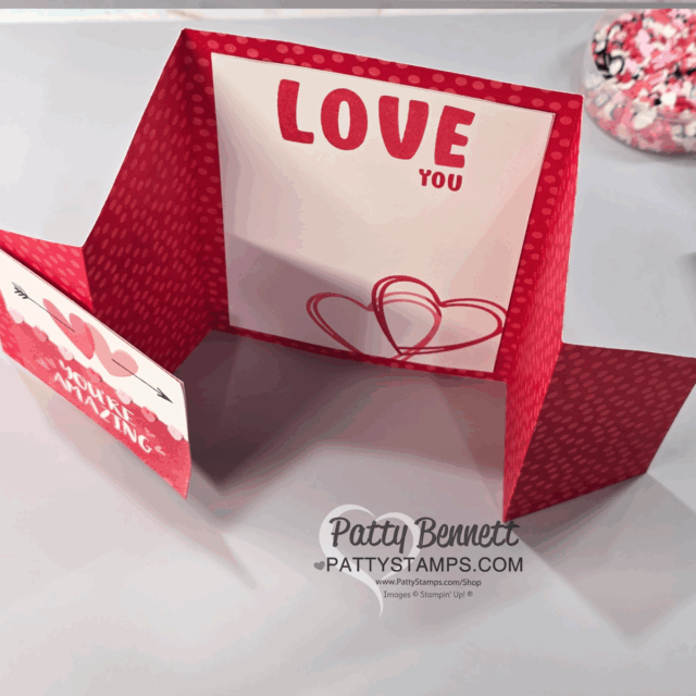 A handmade pop-up Valentine card with red and white heart patterns, featuring a large "LOVE YOU" message inside. Red die-cut hearts decorate the center. Inspired by Fun Fold Cards from Patty Bennett’s Special Live. Watermark at the bottom. To read more, visit Patty Stamps (pattystamps.com)