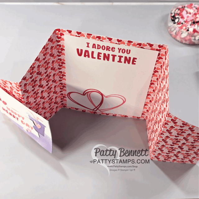 A three-panel Valentine’s Day card, created as a Fun Fold Card, is displayed open. The card features a red heart pattern and a message inside reading “I ADORE YOU VALENTINE” above two interlocking hearts, signed “Patty Bennett.”. To read more, visit Patty Stamps (pattystamps.com)