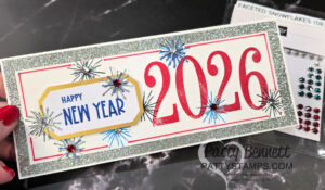 A handmade New Year card with large red "2026" numbers, blue starbursts, silver glitter border, and a yellow label reading "HAPPY NEW YEAR" in blue text. The card is held by a hand with red nails. Faceted snowflake gems are visible in the background. To read more, visit Patty Stamps (pattystamps.com)