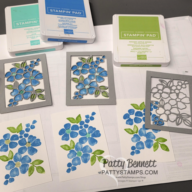 Three ink pads (aqua blue, light blue, and green) sit at the top. Below are rectangular floral die cuts and three stamped cards showing blue flowers with green leaves. Gray metal dies and finished die-cut pieces are also displayed. “PattyStamps.com” is watermarked. To read more, visit Patty Stamps (pattystamps.com)