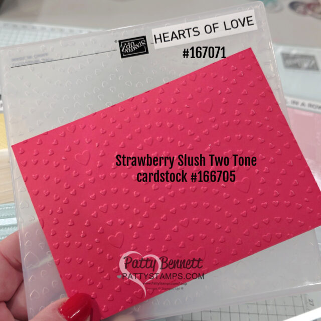 A hand holds a pink Strawberry Slush Two Tone embossed cardstock (#166705) with small hearts and dots, placed against a clear "Hearts of Love" embossing folder (#167071). The Patty Bennett PattyStamps.com logo is visible at the bottom of the cardstock. To read more, visit Patty Stamps (pattystamps.com)