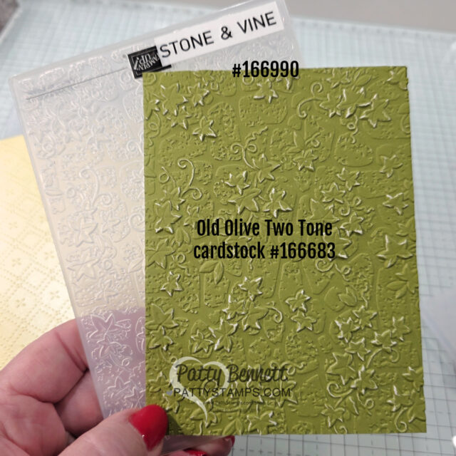 A hand holds a clear embossing folder labeled “Stone & Vine #166990” and a raised, textured green cardstock labeled “Old Olive Two Tone cardstock #166683.” The green card features an embossed vine and floral pattern. The background is a craft workspace. To read more, visit Patty Stamps (pattystamps.com)