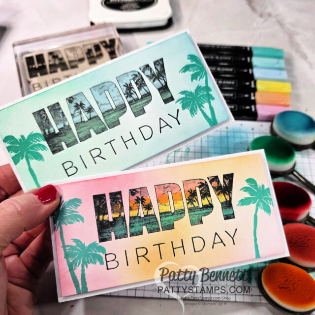 A hand holds two handmade birthday cards, each with "HAPPY BIRTHDAY" in large letters. "HAPPY" is filled with a tropical sunset and palm trees; "BIRTHDAY" is in simple font. Cards are pastel blue and pink, with palm tree graphics. Craft supplies surround them. To read more, visit Patty Stamps (pattystamps.com)