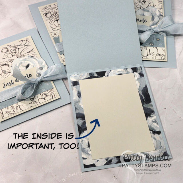 A handmade greeting card in light blue is open, revealing a blank cream panel bordered by floral-patterned paper. An arrow points to the inside with the text, “THE INSIDE IS IMPORTANT, TOO!” Two similar closed cards and a ribbon are also visible in the background. To read more, visit Patty Stamps (pattystamps.com)