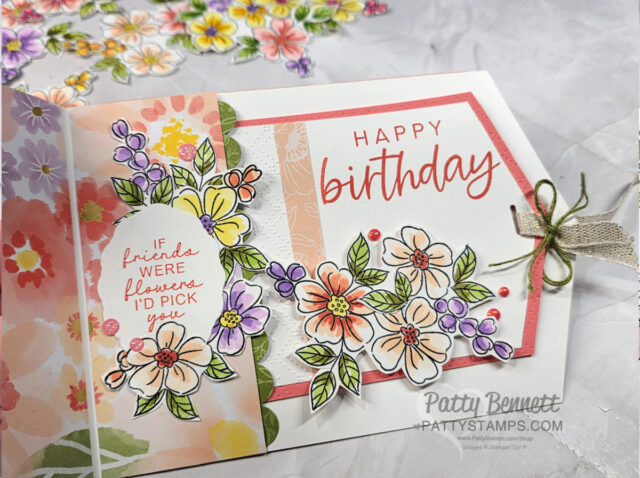 A handmade birthday card features colorful hand-drawn flowers, leaves, and a bow. "Happy birthday" is written in red on a white tag bordered in coral. Another tag reads, “If friends were flowers, I’d pick you.” Floral embellishments and gems decorate the card. To read more, visit Patty Stamps (pattystamps.com)
